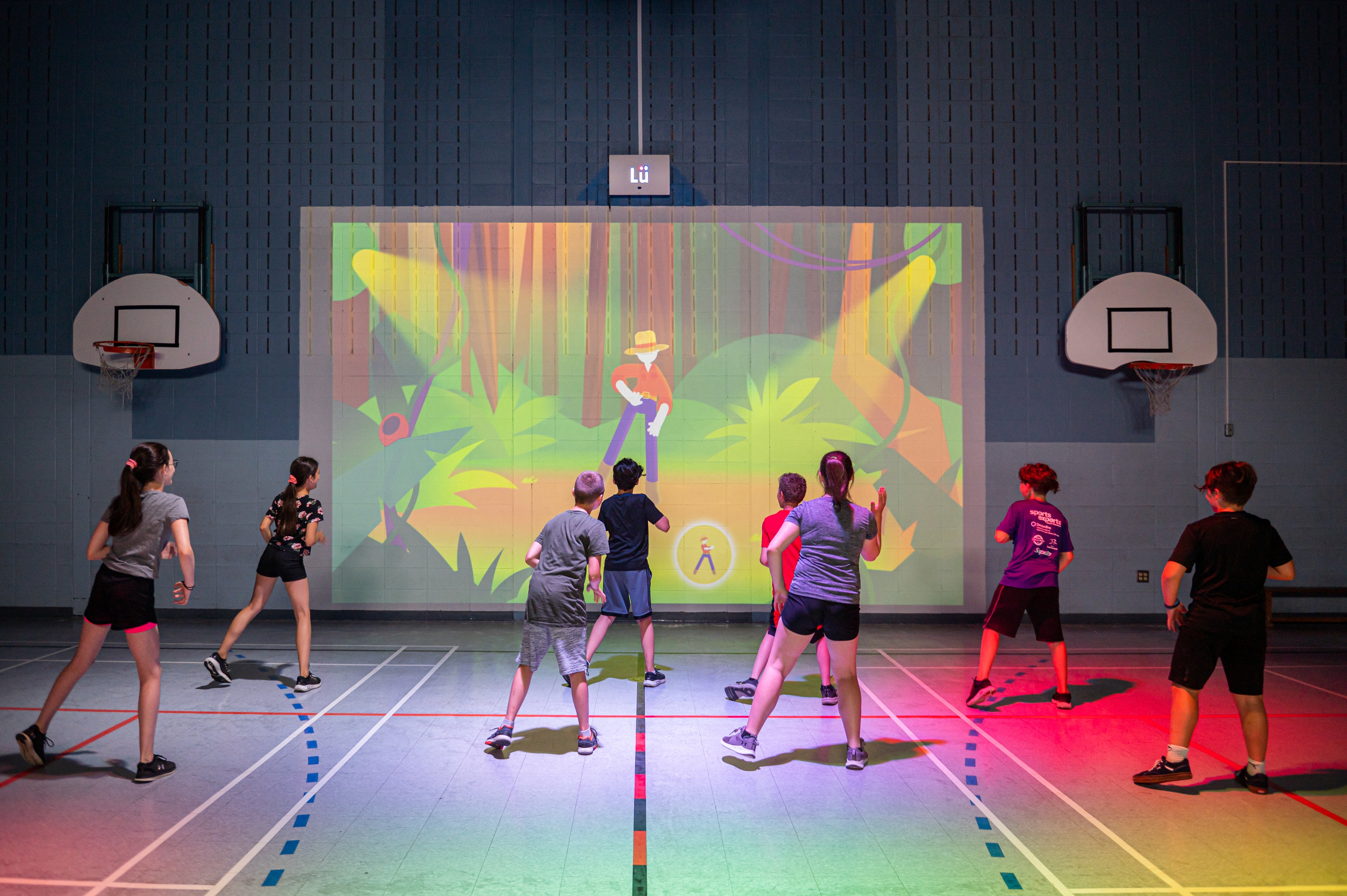 Group of students playing LU-App-Danza on a large screen in an indoor gym.