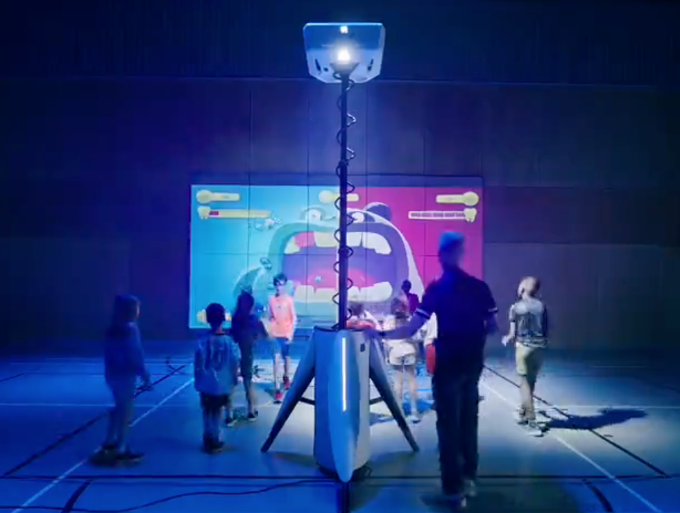 Children and adults gathered around a Play Lü - Möve displaying a colorful graphic.