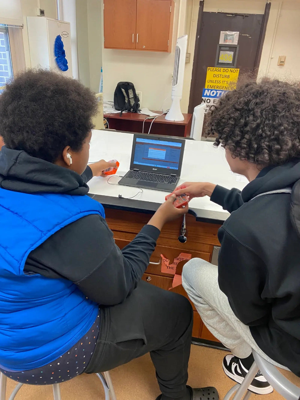 Two students collaborate on a robotics activity using a laptop and handheld devices.